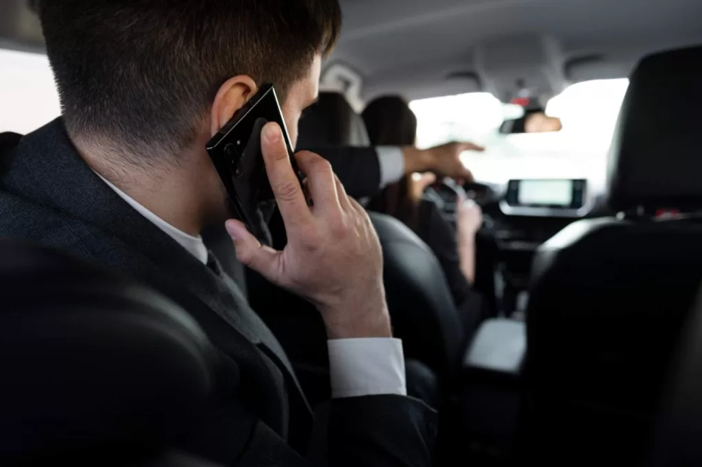 Passenger in a suit talking on the phone inside a taxi, while the driver is driving.